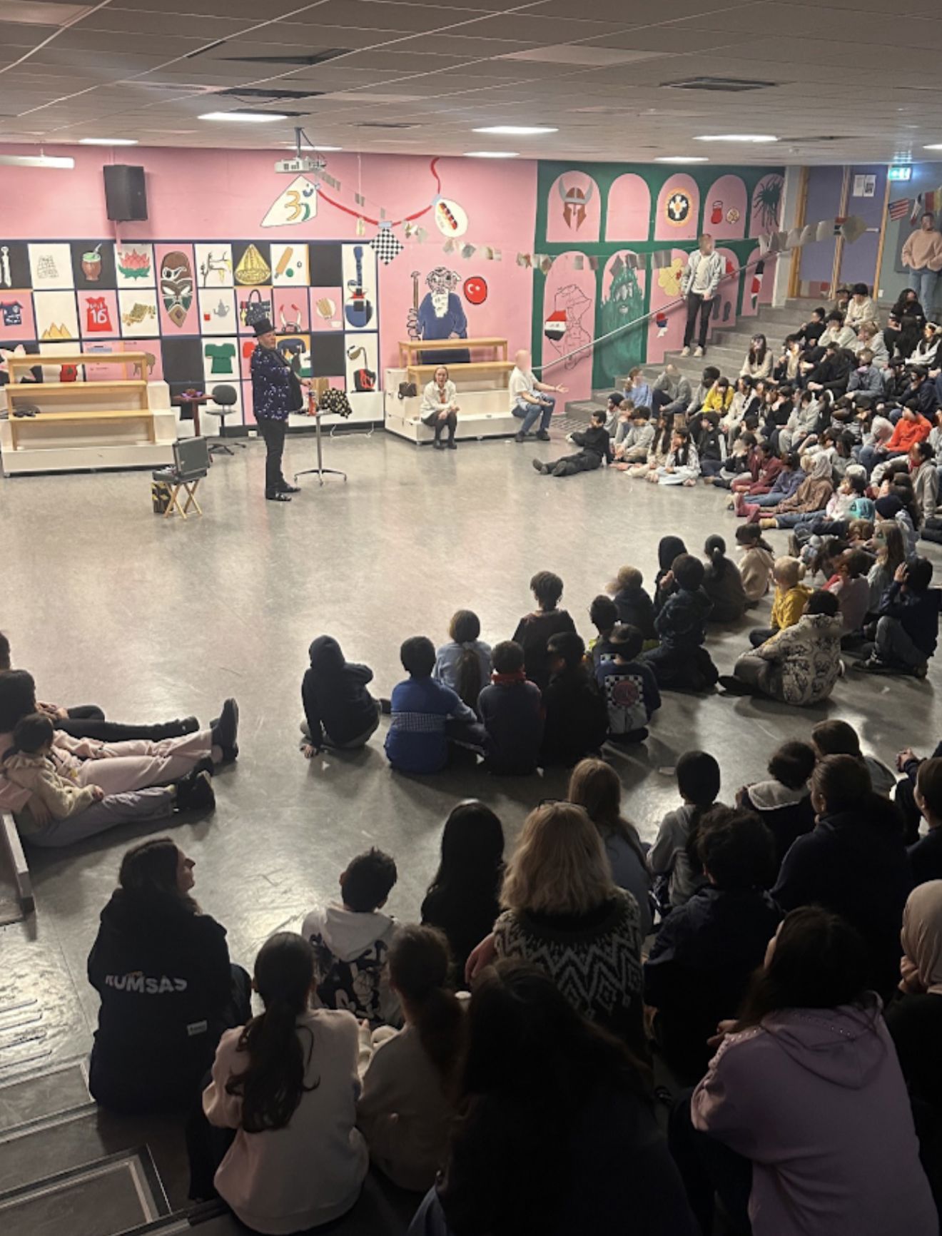 en gruppe mennesker som sitter i et rom med en person som står på en scene en gruppe mennesker som sitter i et rom med en person som står på en scene